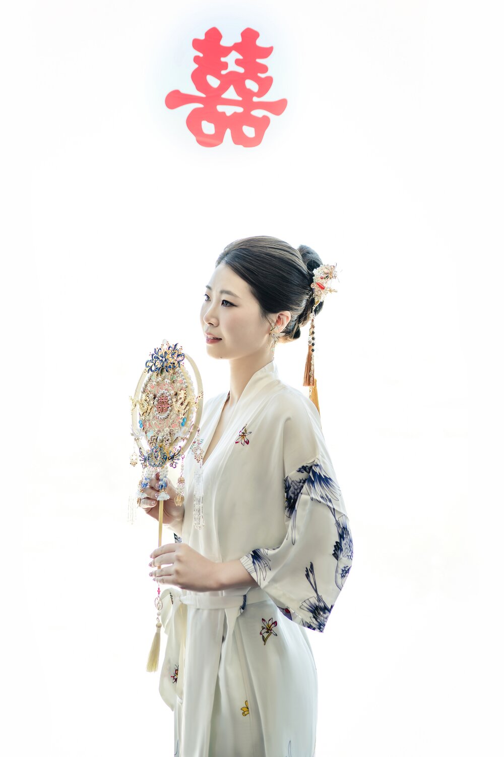 Bride holding a traditional fan beneath a red double happiness sign